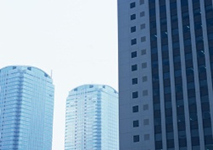 晴れた空を背景に、左に白い高層ビルが隣接し、手前に濃い灰色の高層ビルがあります