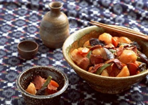 和風柄のランチョンマットの上に大きな器に入った肉じゃがと、小皿に取り分けられた肉じゃががあります。その横にはとっくりとおちょこが並んでいます